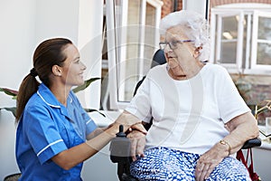 Senior Woman Sitting In Motorized Wheelchair Talking With Nurse In Retirement Home photo