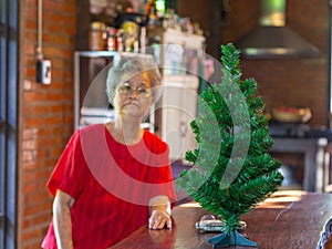 Senior woman sitting near a Christmas tree at home. Concept of aged people and Christmas and happy new year festival