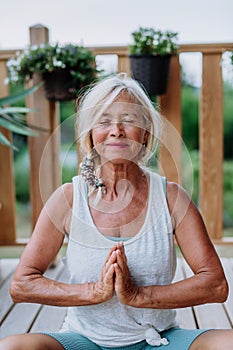 A senior woman sitting outdoors on a terrace in summer, doing yoga exercise.