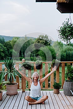 A senior woman sitting outdoors on a terrace in summer, doing yoga exercise.