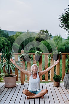 A senior woman sitting outdoors on a terrace in summer, doing yoga exercise.