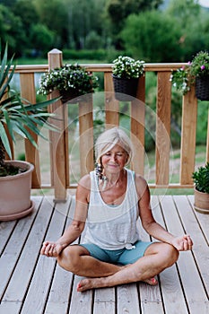 A senior woman sitting outdoors on a terrace in summer, doing yoga exercise.