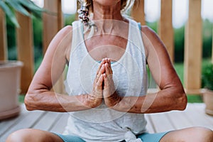 A senior woman sitting outdoors on a terrace in summer, doing yoga exercise,close-up.