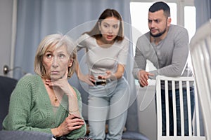 Senior woman sitting on sofa, her son and daughter-in-law quarreling with her