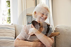 Senior Woman Sitting On Sofa At Home With Pet French Bulldog