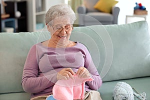 Senior woman sitting on sofa while knitting sweater at home