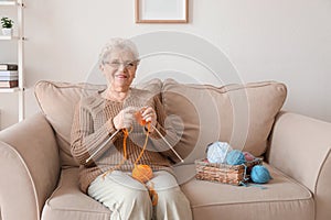 Senior woman sitting on sofa while knitting sweater at home