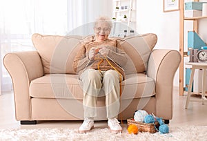 Senior woman sitting on sofa while knitting sweater at home