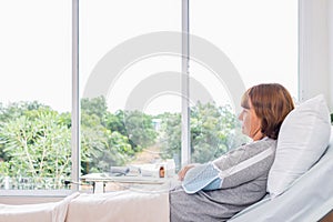Senior woman sitting on sofa in living room at home and looking at window