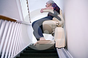 Senior Woman Sitting On Stair Lift At Home To Help Mobility