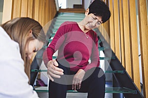 Senior woman sitting on the stairs patiently waiting for nurse to tie up her shoes