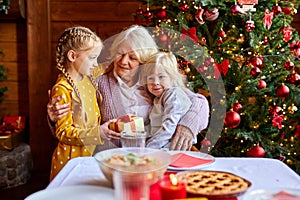 Senior woman sitting at a table with grandchildren, having fun at Christmas dinner