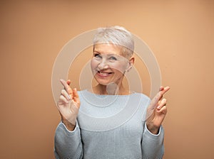 Senior woman with sjort hair thinking about something pleasant and making wish with crossed fingers