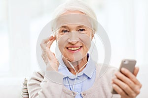 Senior woman with smartphone and earphones at home