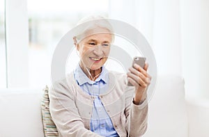 Senior woman with smartphone and earphones at home