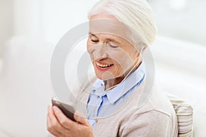 Senior woman with smartphone and earphones at home