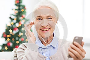 Senior woman with smartphone and earphones at home