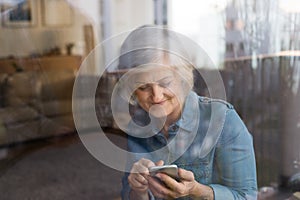 Senior woman with smartphone at home sitting at the window
