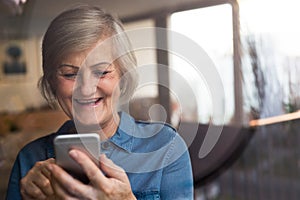 Senior woman with smartphone at home sitting at the window