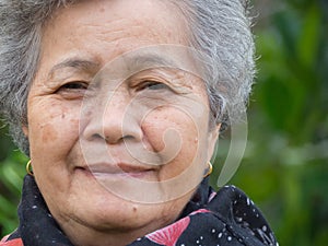 Senior woman smiling and looking at the camera while standing in a garden. Headshot photo. Concept of aged people and healthcare