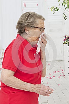 Senior Woman sneewing in a tissue outside.