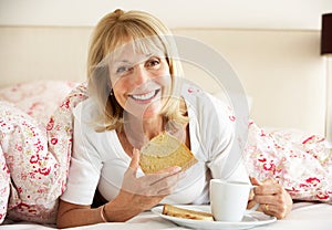 Senior Woman Snuggled Under Duvet Eating Breakfast