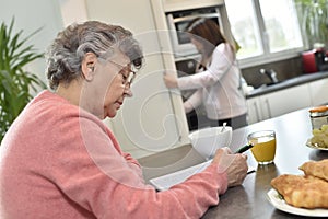 Senior woman spending time doing crosswords with a home helper in the background