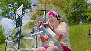 Senior woman after sport training listening music on playground, celebrate win doing winner gesture