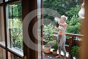 A senior woman with sports bra outdoors on a terrace in summer, drinking water.