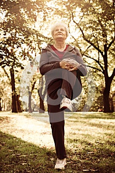 Senior woman in sports clothing exercising in park.