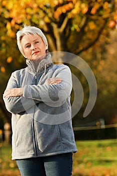 Senior woman standing with crossed arms in autumn high size