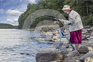 A senior woman standing with her walker by the lake and fishing