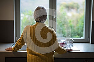 Senior woman standing near the kitchen sink and looking through window