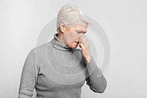 Senior woman standing with nose closed on grey background