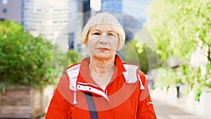 Senior woman standing outdoors. Downtown business dictrict with skyscrapers and trees on background