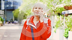Senior woman standing outdoors using smartphone. Downtown business dictrict on background