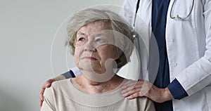 Senior woman staring at camera, caring nurse standing nearby, closeup