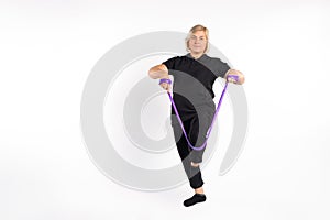 Senior woman stretches elastic band with her leg, on white empty space. Healthy, pandemic concept