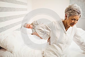 Senior woman suffering from backache sitting on bed