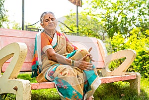 Senior woman suffering from kee joint pain after walking while sitting at park - concept of arthritis, unhealthy and