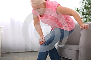 Senior woman suffering from knee pain in living room.