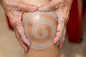 Senior woman suffering from knee pain sitting on chair, Massaging by her hand, Body concept