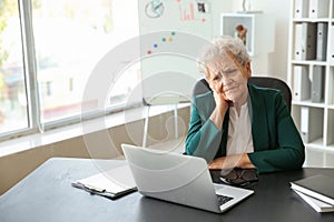 Senior woman suffering from neck pain while sitting at table with laptop