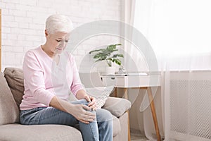 Senior woman suffering from pain in leg, massaging her knee photo