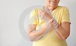 Senior woman suffering from pain in wrist on light background