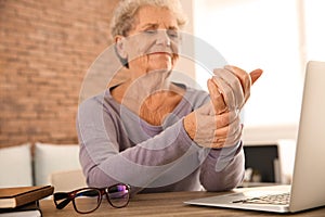 Senior woman suffering from pain in wrist while sitting at table with laptop