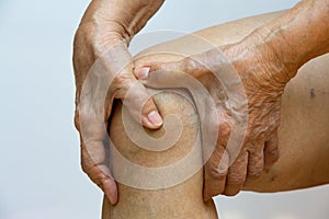 Senior woman suffering from right knee pain, Massaging by her hand in white background, Close up & Macro shot, Asian body skin