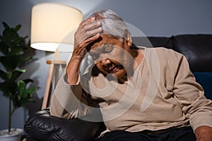 senior woman suffering from stress or a headache while sitting on sofa in living room at night