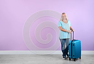 Senior woman with suitcase near color wall