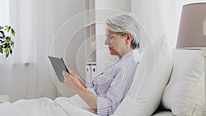 Senior woman with tablet pc in bed at home bedroom